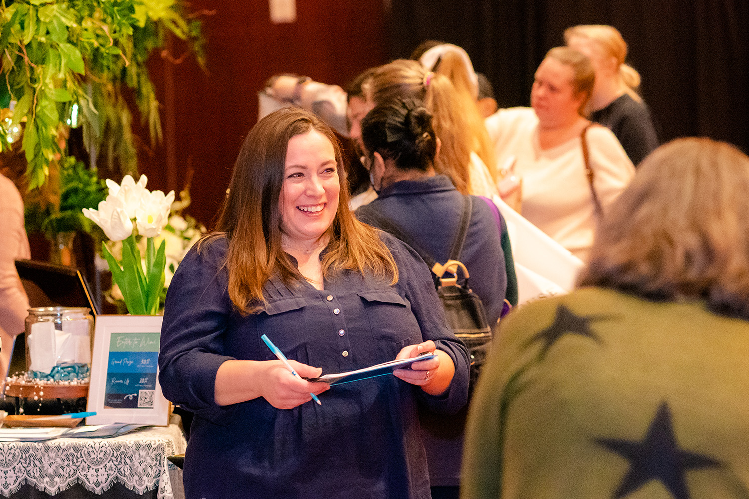 A woman holding a clipboard and pen at a wedding show.